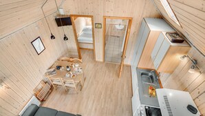 Una habitación pequeña con suelo de madera, zona de comedor, kitchenette y un rincón de estar.