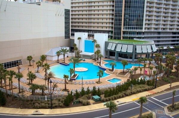 Un hôtel doté d’une grande piscine centrale, entourée de palmiers et de chaises longues.