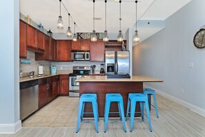 Une cuisine moderne avec des meubles en bois, des appareils en acier inoxydable, un îlot central doté de tabourets et un éclairage suspendu.