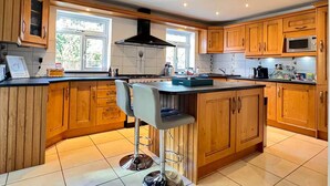 A spacious kitchen with wooden cabinets, a central island with bar stools, a stove, and a microwave. - Comfortable 6 Guest Home - Walk to Canal & Award-Winning Pub (Weston-on-Trent)