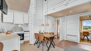 A modern kitchen with white cabinetry, a dining area with a wooden table and chairs, and a view of greenery outside. - Lovely home in Tranekær (Tranekær)