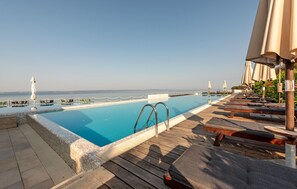 Ein Poolbereich mit Liegestühlen und Sonnenschirmen, mit Blick auf das klare Meer und einer Holzterrasse.