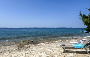 Une plage dallée de pierres, avec des chaises longues et une vue dégagée sur la mer.