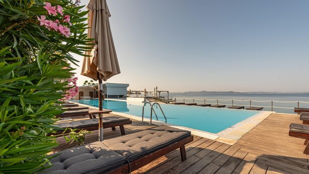 Un área junto a la piscina con sillones de descanso, una terraza de madera y vista al mar.