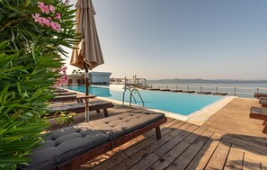 Un área junto a la piscina con sillones de descanso, una terraza de madera y vista al mar.