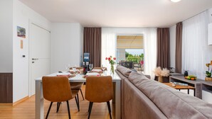 Un comedor moderno con una mesa preparada para cuatro comensales, dos sillas, un sofá y vistas al exterior.