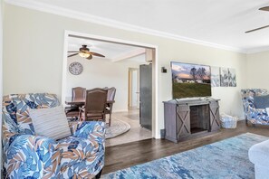 Ein Wohnzimmer mit einer Couch, einem Couchtisch und einem TV-Schrank. Es gibt einen Essbereich mit Tisch und Stühlen.
