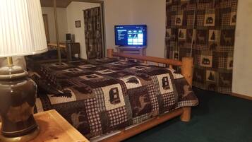 Ein Schlafzimmer mit einem hölzernen Bett, einem Fernseher auf einem Schrank, einer Lampe und gemusterten Vorhängen.