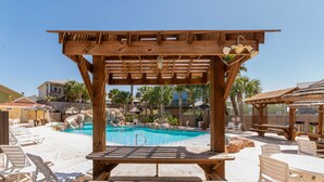 Een houten pergola met een zwembadgedeelte, inclusief ligbedden en picknicktafels.