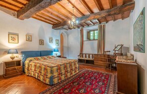 Ein traditionell eingerichteter Raum mit Holzbalkendecke, einem Bett mit gemustertem Überwurf, einem Holzschrank, einem Spiegel und einem roten Teppich mit Muster.