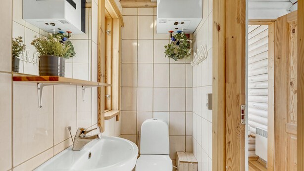 A small bathroom with a white sink, toilet, and wooden shelving. - Lovely home in Tranekær (Tranekær)