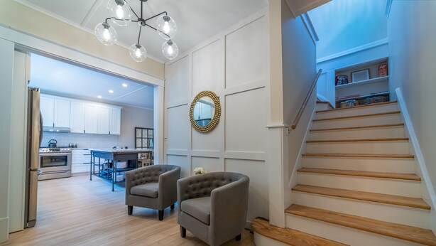Un salon moderne avec un escalier, un plancher en bois et un coin repas à l’arrière-plan.