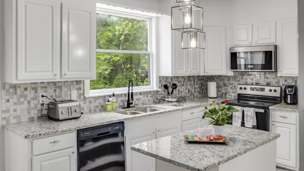 A modern kitchen with white cabinets, a granite countertop, a stainless steel oven, and a window with a view of greenery.