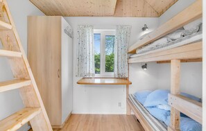 Une chambre à coucher de taille réduite, avec un lit superposé, une petite fenêtre ornée de rideaux à motifs floraux, une échelle en bois et une étagère en bois.
