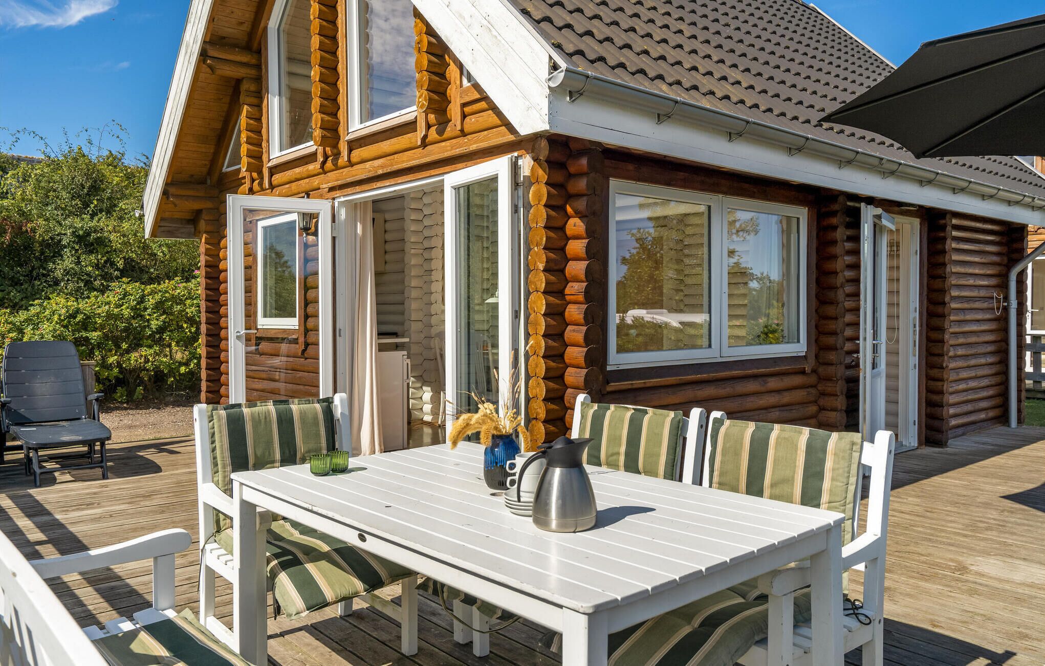 A wooden cabin with a deck, featuring a table and chairs, and large windows.