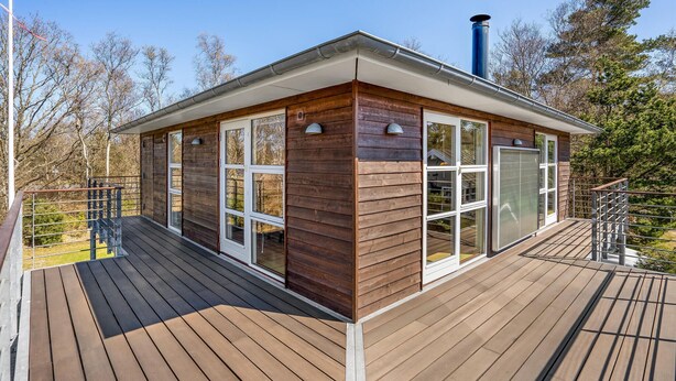 Une cabane dotée d’une terrasse, de grandes fenêtres et d’une cheminée.