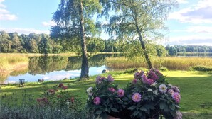 A serene lakeside garden with a pond, lush greenery, and a large potted flower arrangement in the foreground.