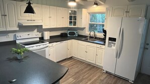 A kitchen with white cabinets, a black countertop, a stove, a sink, and a refrigerator.