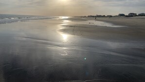 A beach with a calm sea, a clear sky, and distant buildings.