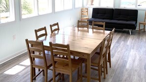 A spacious room with a large wooden dining table surrounded by chairs, a black sofa, and a ceiling fan.