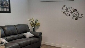 A living room with a dark leather sofa, a patterned rug, a small table, and a decorative wall piece. - Adorable 1 bed room legal basement suite (Saskatoon)