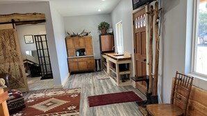 Un salón amplio con suelo de madera, un mueble grande de madera, un televisor y una zona de comedor con una silla y mesa de madera.