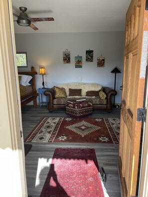 Ein Wohnzimmer mit einem braunen Sofa, einem gemusterten Hocker, einem roten Teppich und einem Deckenventilator.
