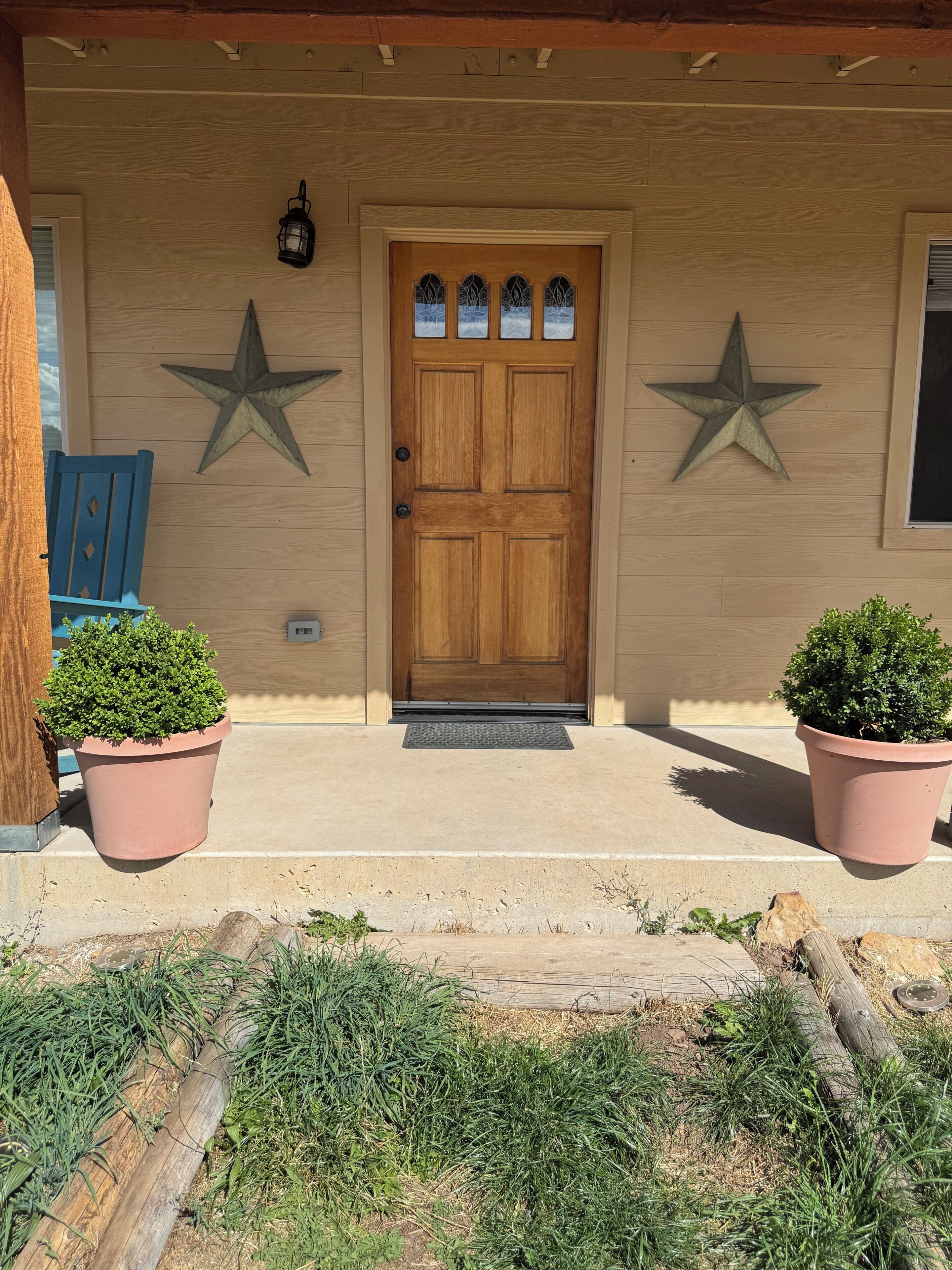 Uma porta de madeira com painéis de vidro decorativos, dois vasos de plantas de cada lado e duas estrelas na parede.