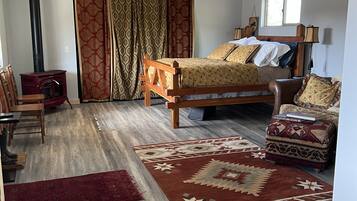 Un dormitorio con una cama, una silla de madera, una mesita, un calentador, una ventana y un ventilador de techo.