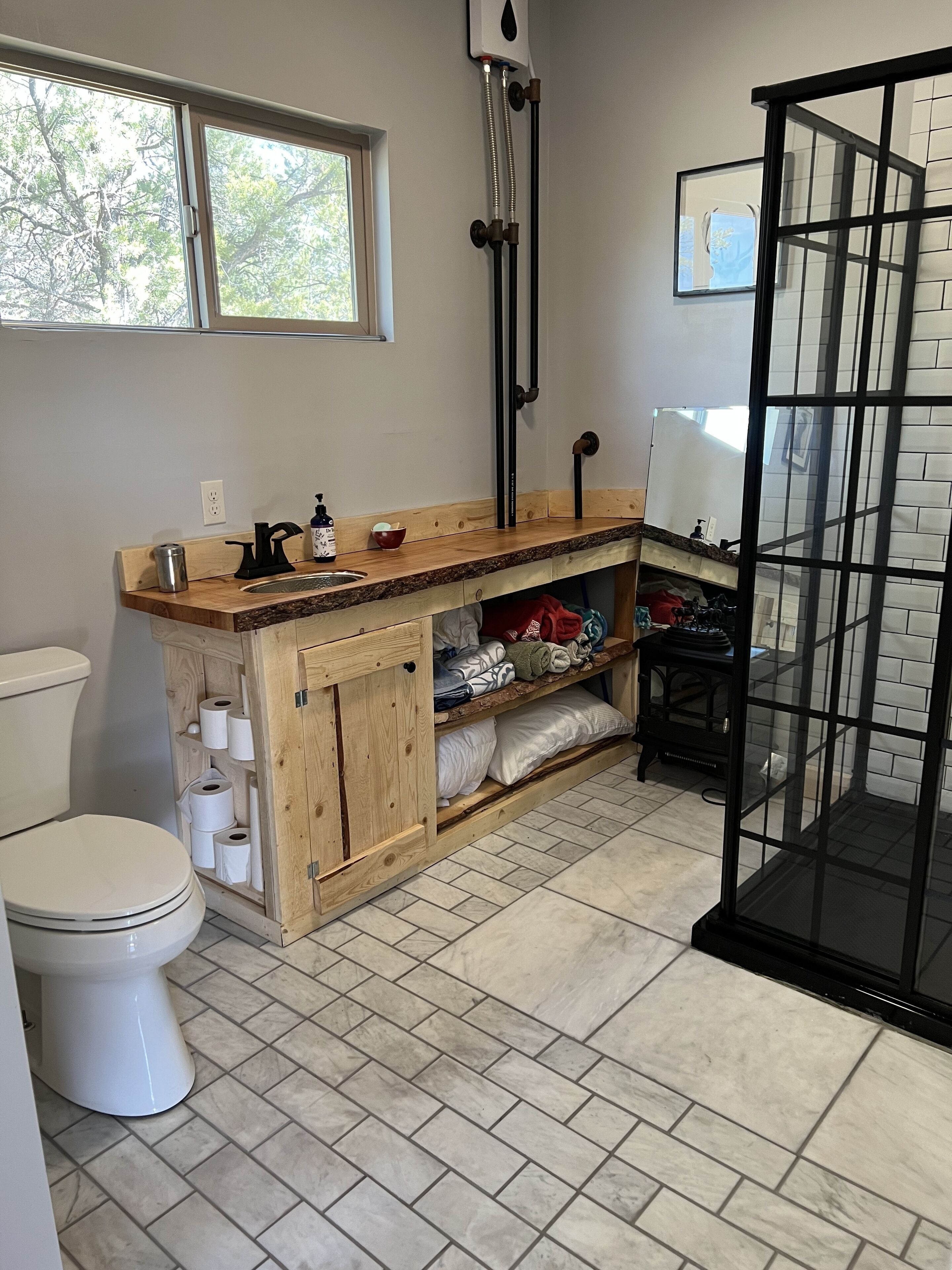 A bathroom with a toilet, wooden cabinet with towels, a sink with a mirror, and a shower area.