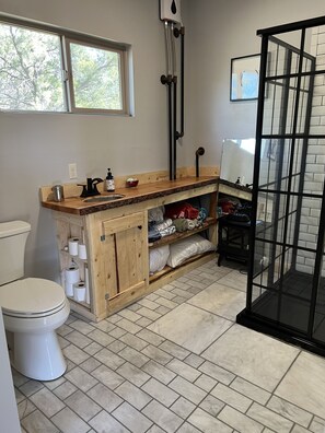 Ein Badezimmer mit Toilette, Holzschrank mit Handtüchern, Waschbecken mit Spiegel und Duschbereich.