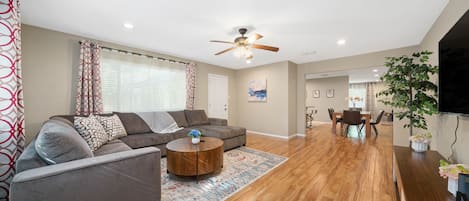 A spacious living room with a grey sofa, round coffee table, and a patterned rug.