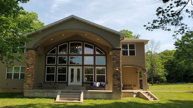 A two-story house with a stone facade, large windows, and a covered porch. - Secluded Lakefront Retreat on 60 Acres Private Dock, Fishing & Wildlife (Gravois Mills)