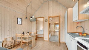 Interior acogedor de una cabaña de madera con comedor, kitchenette y un baño visible a través de una puerta abierta.