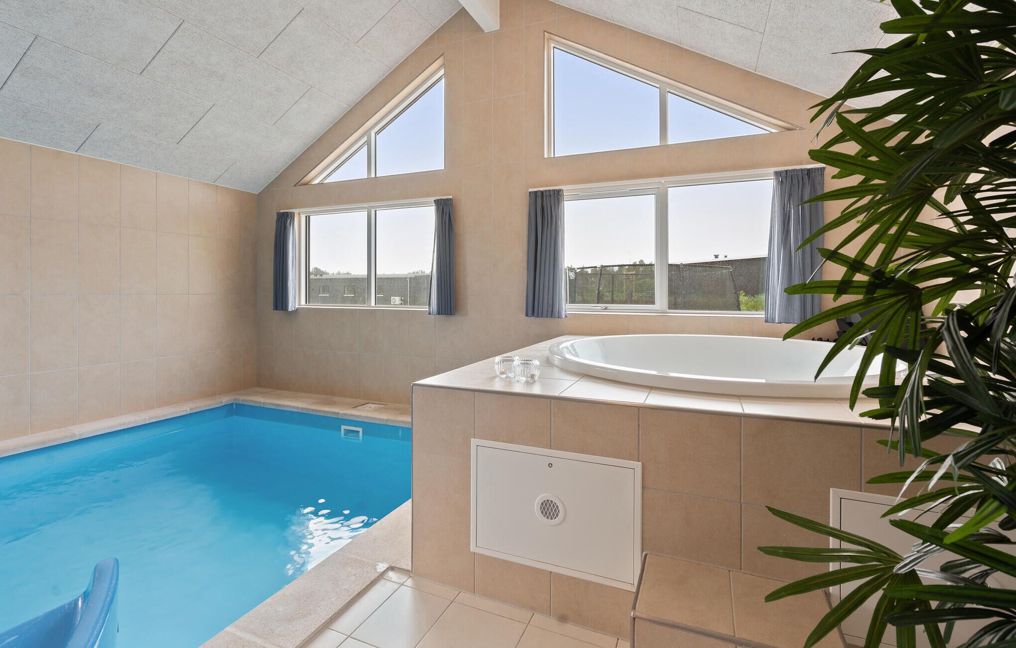 Een modern binnenzwembad met een jacuzzi, grote ramen en uitzicht op het omliggende landschap.