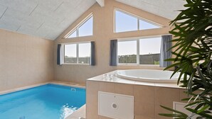 Une piscine intérieure moderne, dotée d’un jacuzzi, de grandes fenêtres et offrant une vue sur l’extérieur.