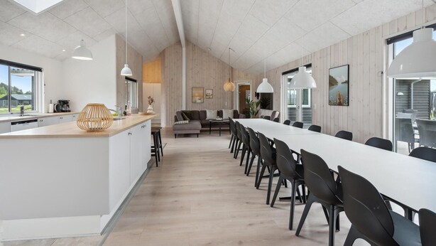 Une cuisine moderne dotée d’un grand îlot central, un coin repas avec une longue table et des chaises, et un espace de vie comprenant un canapé et une table basse.