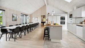 Une cuisine spacieuse dotée d’un grand îlot central, d’appareils électroménagers modernes et offrant une vue sur un coin repas avec une piscine.