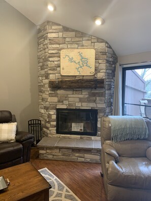 A stone fireplace with a map above it, a leather sofa, and a wooden coffee table in a living room.