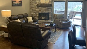 A living room with a stone fireplace, leather sofas, a coffee table, and a ceiling fan. - 2 bedroom condo in osage beach (Osage Beach)