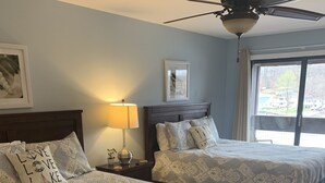 A bedroom with two beds, a ceiling fan, a window with a view, and a nightstand with a lamp. - 2 bedroom condo in osage beach (Osage Beach)