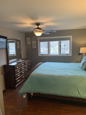 A bedroom with a bed, dresser, ceiling fan, window, and wall decorations.