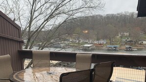 A covered outdoor patio with a round table and wicker chairs, overlooking a lake with boats and houses. - 2 bedroom condo in osage beach (Osage Beach)