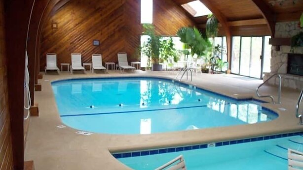 An indoor swimming pool with a wooden ceiling, lounge chairs, and potted plants. - 2 bedroom condo in osage beach (Osage Beach)