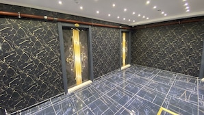 Ein Raum mit schwarzen Marmorwänden und -boden, ausgestattet mit zwei Türen mit goldenen Griffen und einer modernen Decke mit eingelassener Beleuchtung.