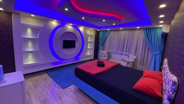 Ein modernes Schlafzimmer mit einem Bett, zwei Stühlen, einem Fernseher und einem kleinen Tisch.