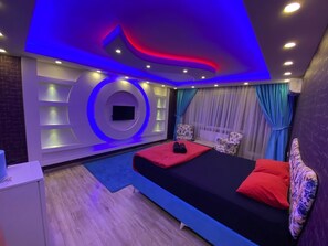 Une chambre moderne avec un lit, deux fauteuils, une télévision et une petite table.