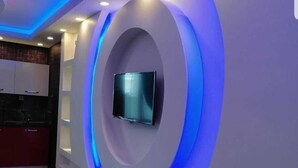 Ein modernes Interieur mit einem an einer gewölbten Wand montierten Fernseher, eingelassener Beleuchtung und Holzboden.