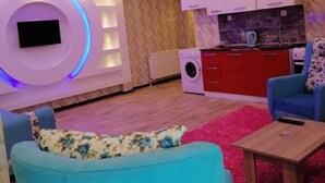 Ein modernes Wohnzimmer mit Flachbildfernseher, einer Couch, einem Couchtisch und einer Küchenzeile mit roten Schränken und einer Waschmaschine.