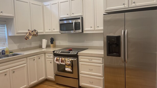 Una cocina con armarios blancos, un refrigerador de acero inoxidable, un microondas y un horno.